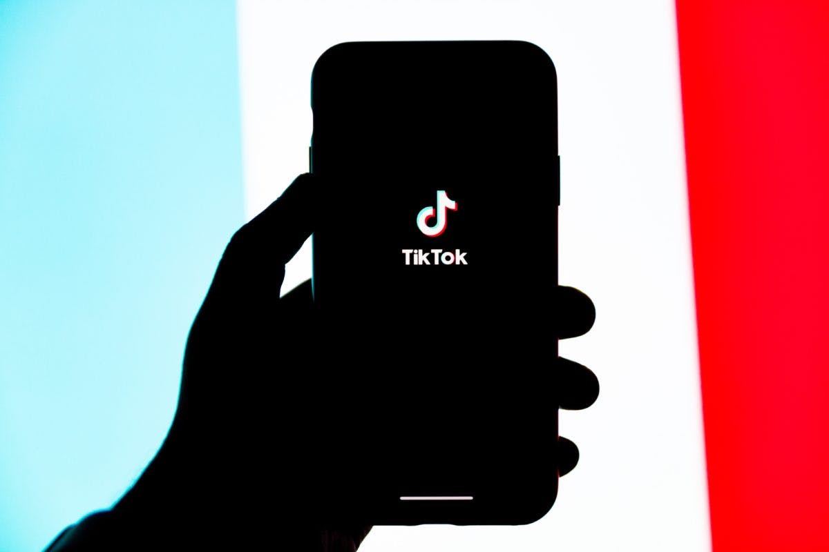 TikTok growth strategy starts with using the app, here seen on the screen of a cell phone set against a background of blue, white, and red.